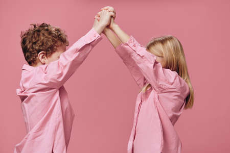 cute, beautiful, joyful children, a boy and a girl play with each other holding hands, standing in pink clothes on a pink background. Horizontal studio photographyの写真素材