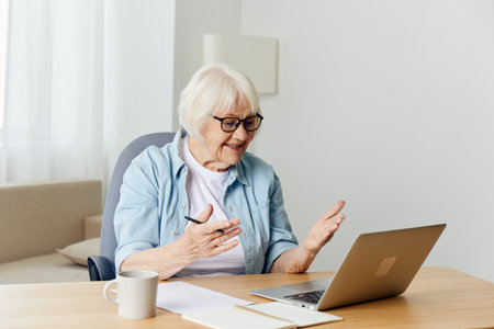 a joyful elderly woman works from home at a laptop and throws up her hands in happiness