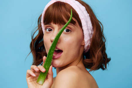 a sweet, happy woman stands on a blue background holding a sprig of aloe vera in her hand and presenting it to her face, happily smiling enthusiastically opening her mouth wideの写真素材