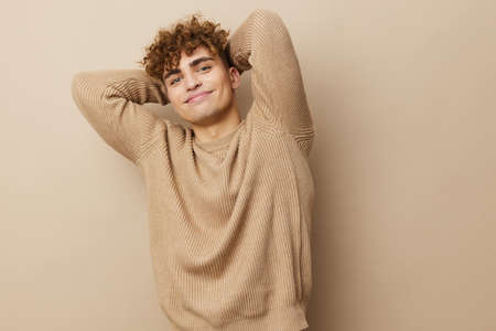 a charming, handsome man stands on a beige background in a sweatshirt and looks at the camera with a...