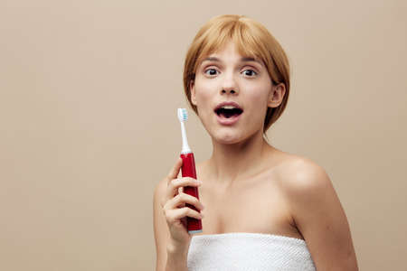 cheerful woman stands with surprised face looking at camera and holding a red electric brush in her hand. Horizontal photo with an empty space on the background for inserting an advertising layoutの写真素材