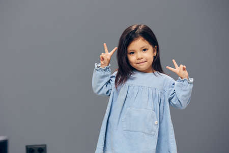 a little girl in a blue dress shows a sign of victory with her handsの写真素材