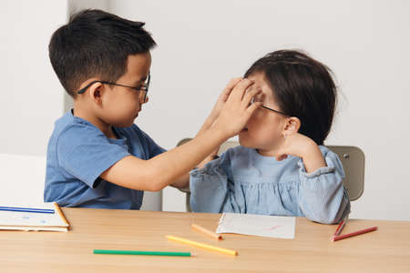 cute little kids are sitting together at the table and the boy is adjusting the girls glassesの写真素材