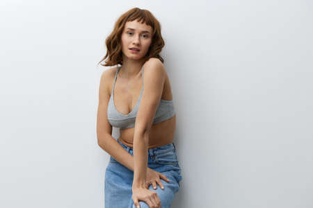 a beautiful, tanned, attractive woman stands on a white background in stylish summer clothes and poses relaxed. Horizontal studio photo with an empty space for inserting an advertising layoutの写真素材