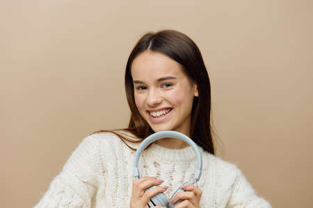 a funny, funny woman in a white sweater stands fooling around with headphones holding them near her faceの写真素材