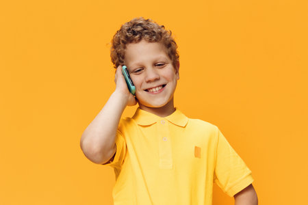 a boy of school age is talking on the phone while standing on a yellow background in yellow clothes. Horizontal photo with space for advertising mockupの写真素材