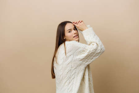 a beautiful, sweet, relaxed, attractive woman stands sideways in a white sweater, posing on a beige...