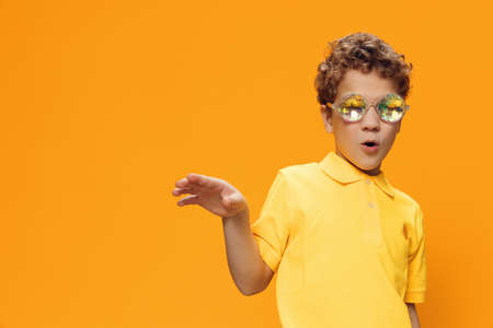 a funny, cute, curly-haired boy stands in yellow clothes on a yellow background in bright, shiny...