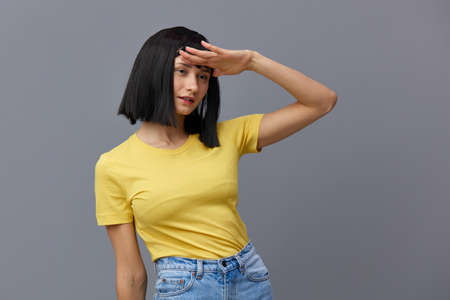 a beautiful, attractive happy woman poses standing on a gray background in a yellow T-shirt and...