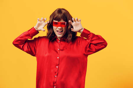 a funny, funny, playful woman stands on a yellow background in a red shirt and fashionable glasses...