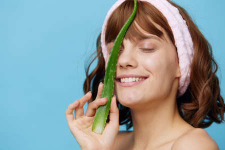 a sweet, happy woman stands on a blue background holding a sprig of aloe vera in her hand and presenting it to her face, smiling happily, closing her eyes with pleasureの写真素材