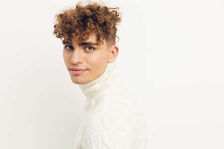 a close horizontal photo of a handsome, attractive man with curly hair, standing in a white knitted...