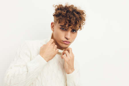 a close photo of a handsome, attractive man with curly hair, standing in a white knitted sweater on...