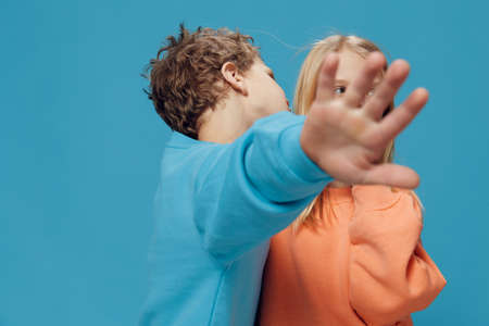 cute, beautiful children, brother and sister stand in bright clothes on a blue background and the girl screams loudly, looking at the camera. Studio photography with blank space for advertising mockupの写真素材