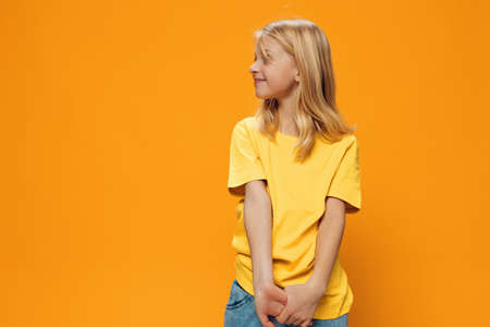 a cute, shy, beautiful school-age girl in yellow clothes stands against a bright, yellow background....