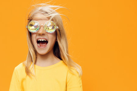 funny, playful girl posing standing on a bright background in yellow clothes and shiny, carnival glasses for a partyの写真素材