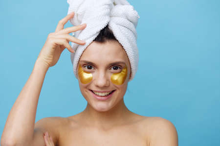Horizontal photo, a woman with radiant skin on a blue background with a towel on her head and body takes care of her face and body in the evenings and relaxes. High quality photoの写真素材