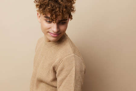 a handsome, attractive man with curly hair, in stylish clothes stands on a beige background and poses relaxedの写真素材