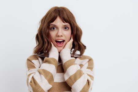 a beautiful, pleasant, emotional woman in a striped sweater looks at the camera standing on a white...