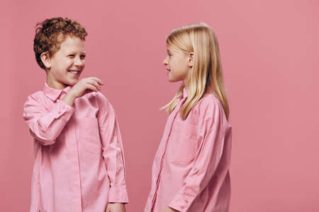 two beautiful children a boy and a girl stand in pink clothes on a pink background and look at each other sweetlyの写真素材
