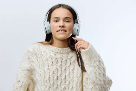 a joyful, relaxed woman in a white sweater stands on a light gray background in the studio listening...