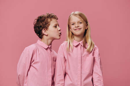 cute, beautiful children are standing in pink clothes on a pink background and the boy reaches out to kiss the girl on the cheek. The topic of relationshipsの写真素材