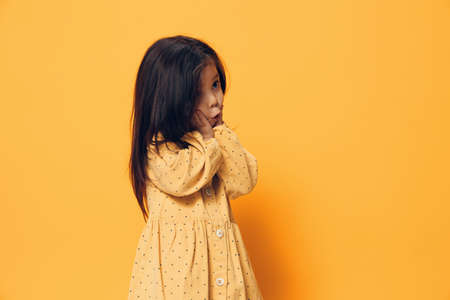 a cute little girl of preschool age stands on an orange background in an orange dress, actively...