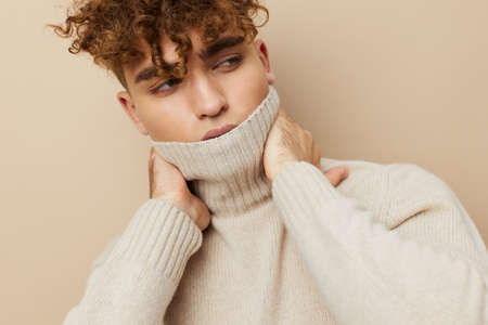 a close portrait of a handsome, attractive man with curly hair, in a light turtleneck pulled over his face, holding his hand on his neckの写真素材