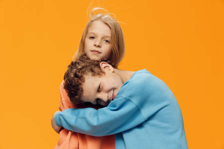 cute, joyful, loving school-age children stand on a yellow background and gently hug each other. theme of friendship and relationshipsの写真素材