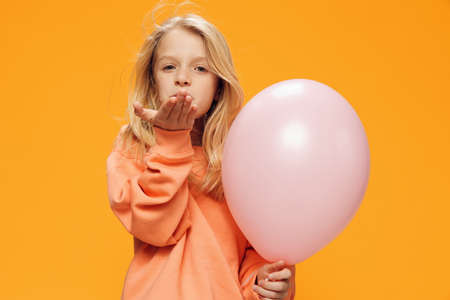 a cute, beautiful school-age girl stands on a bright background with a balloon and sends an air kiss...