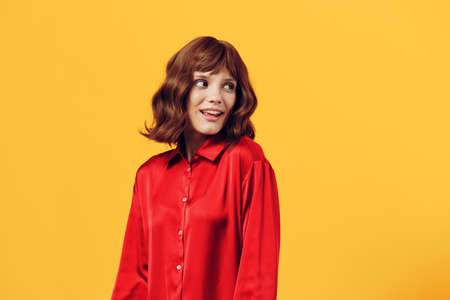 a pleasant, charming woman stands in a stylish red shirt on a yellow background and looks away smiling sweetly. Horizontal photo with an empty space for inserting an advertising layoutの写真素材