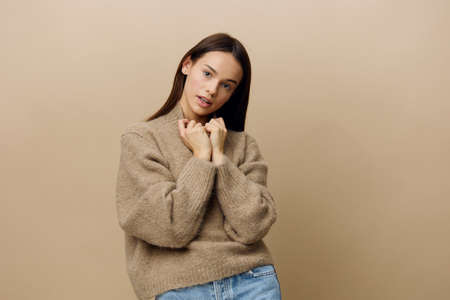 a beautiful, attractive, relaxed woman stands on a beige background in a warm, textured sweater and pulls the neck with her handsの写真素材