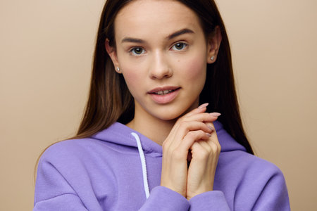 a close, horizontal, studio photograph of a beautiful, pleasant, relaxed woman with neat daytime makeup, looking into the camera and holding her hands in a gentle gesture near her faceの写真素材