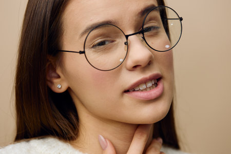 a pretty woman stands on a light background in a white sweater and holds her black glasses with her...