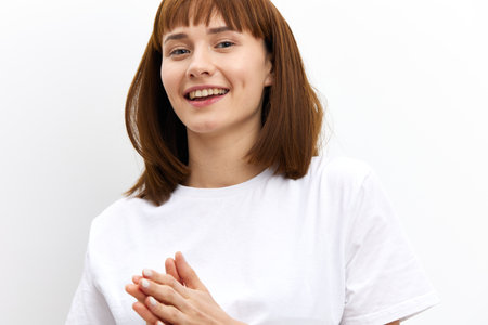 a sweet, happy woman smiles pleasantly looking at the camera standing in a white T-shirt on a light...