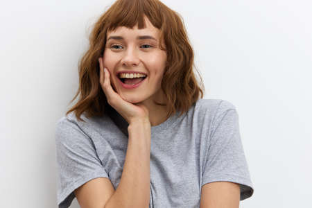 a funny, sweet woman is standing in a gray T-shirt on a white background and smiling broadly looks...