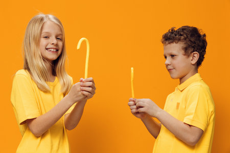 happy children, brother and sister, stand in bright yellow clothes sideways to the camera and joyfully laugh looking at each other. Studio horizontal photography on orange backgroundの写真素材