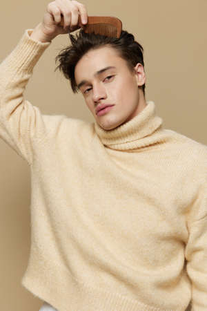 A likable man with light white skin, with a comb in his hands combing his hair back, in a beige...