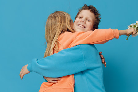 children stand on blue background in bright clothes and happily hug each other holding a bouquet of...