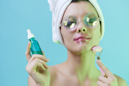 Horizontal photo, a woman with clean skin on a blue background in a towel on her head and body and beautiful glasses and patches on her lips takes care of her face and bodyの写真素材
