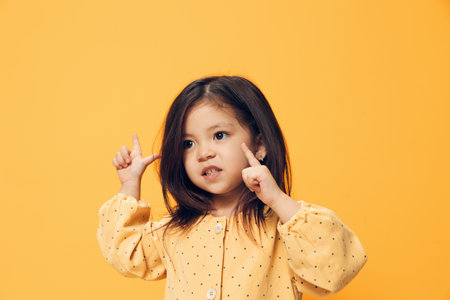 a happy, funny little girl of preschool age stands on an orange background in a trendy dress and...