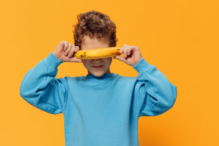funny little boy of school age stands covering his face with a bananaの写真素材