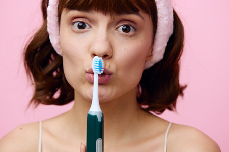 Horizontal studio shot.Close up. A young woman with white skin, a beautiful smile and dark beautiful hair stands on a pink background with a beautiful bandage on her head with a toothbrush.の写真素材
