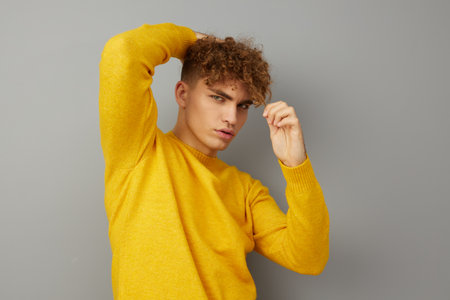 a charming young man stands on a gray background smiling pleasantly, looking away, holding his hand...