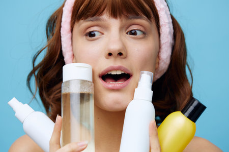 a close horizontal photo on a beauty theme, of a pleasant young woman with clean skin, holding jars of care products in her hands and smiling broadly looking awayの写真素材