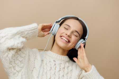 a happy, beautiful woman poses relaxed standing on a background with headphones and gently touches her hands with her eyes closed with pleasureの写真素材