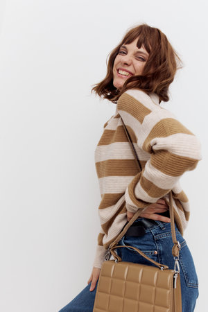 a sweet, attractive woman is standing in a stylish sweater, with a bag on her shoulder and smiling pleasantly at the camera with her hand on her belt.の写真素材