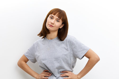 joyful woman with red hair and a beautiful hairstyle looks at the camera smiling and keeps her hands...