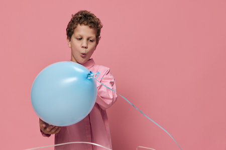 happy, funny boy in pink clothes on a pink background plays joyfully smiling with a blue balloonの写真素材
