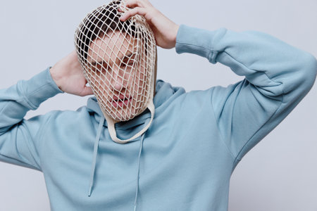a close horizontal photo of a sad, tired man with a mesh on his face, holding his hands on his head